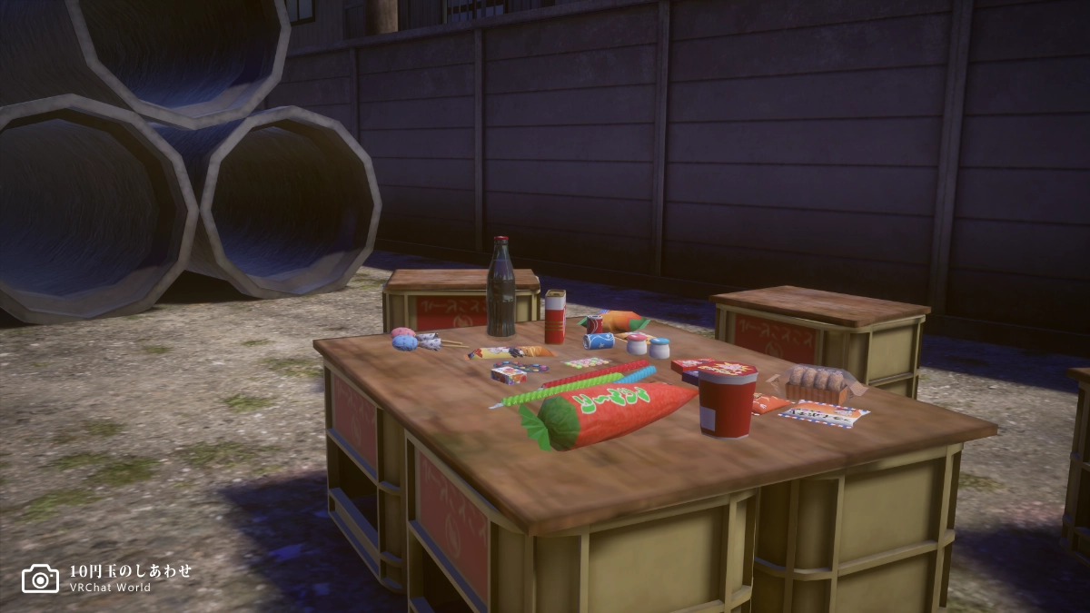 「10円玉のしあわせ」駄菓子屋の前にある空き地。土管の横に子供たちが配置したであろうビールケース製のテーブルに駄菓子が置かれています。